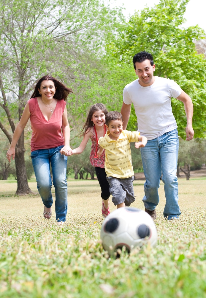 Parents and two young children playing soccer in the green field, outdoor